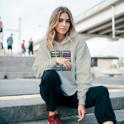 Woman wearing a grey retro cassette tape graphic hoodie with vintage 90s music design paired with black pants and red sneakers in an urban setting.