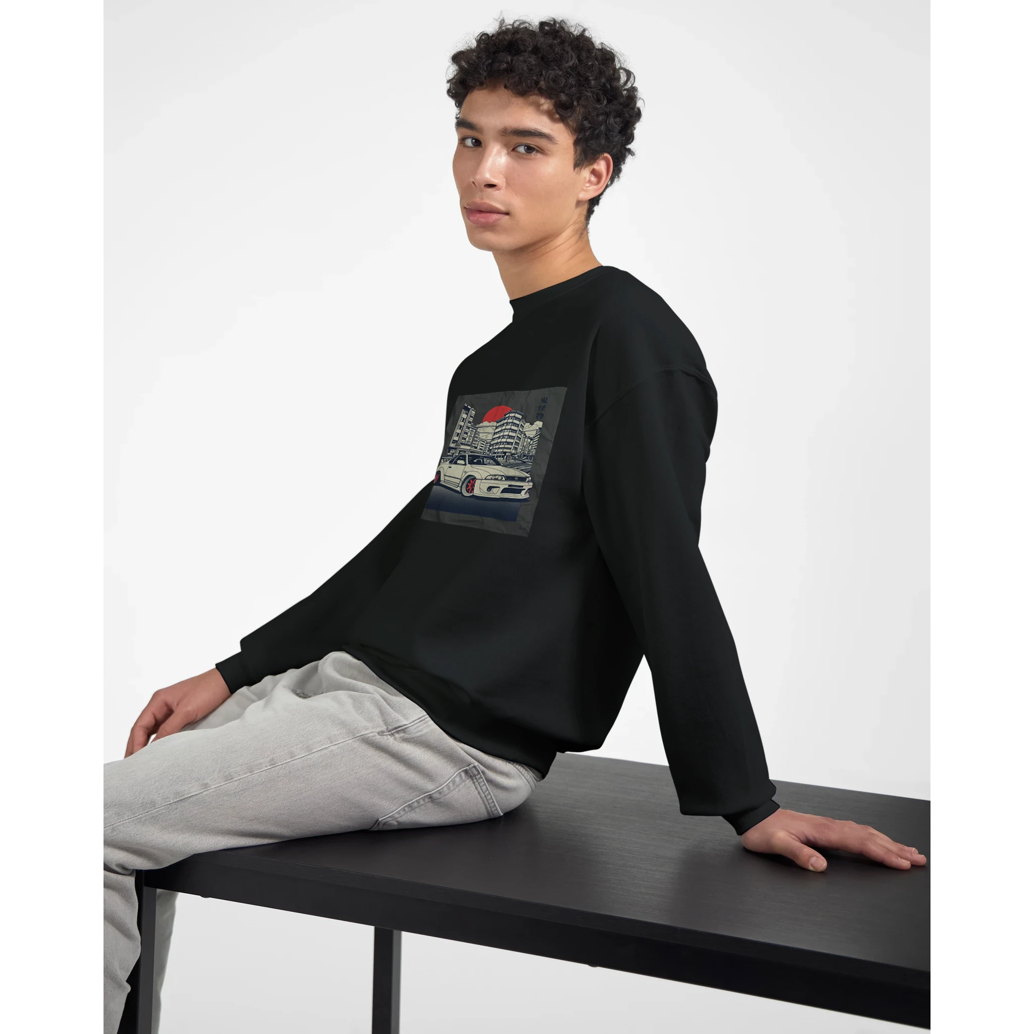 Young man wearing a black 50/50 cotton-poly Car Jumper JDM sweatshirt with a car graphic, seated at a table.