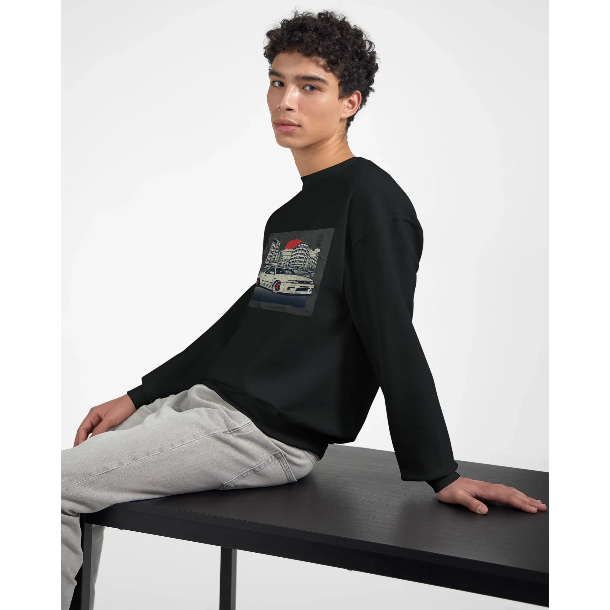 Young man wearing a black 50/50 cotton-poly Car Jumper JDM sweatshirt with a car graphic, seated at a table.