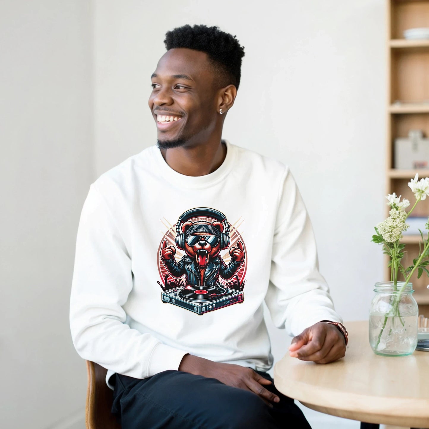 Man wearing a white men's graphic sweatshirt with a graphic design, sitting in a casual setting.