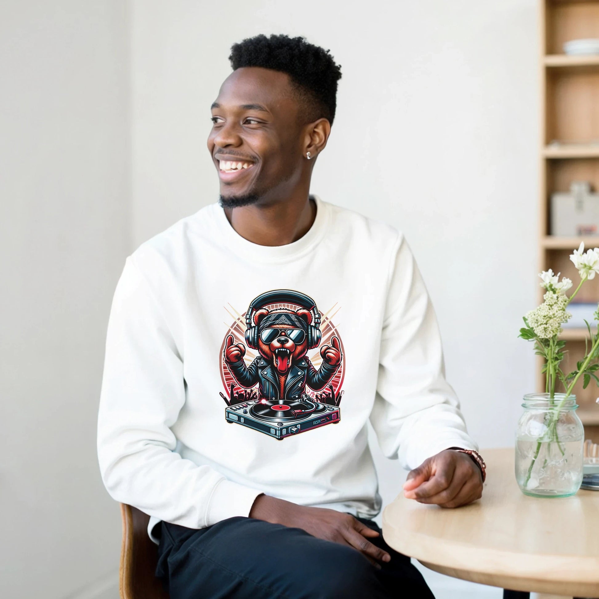 Man wearing a white men's graphic sweatshirt with a graphic design, sitting in a casual setting.