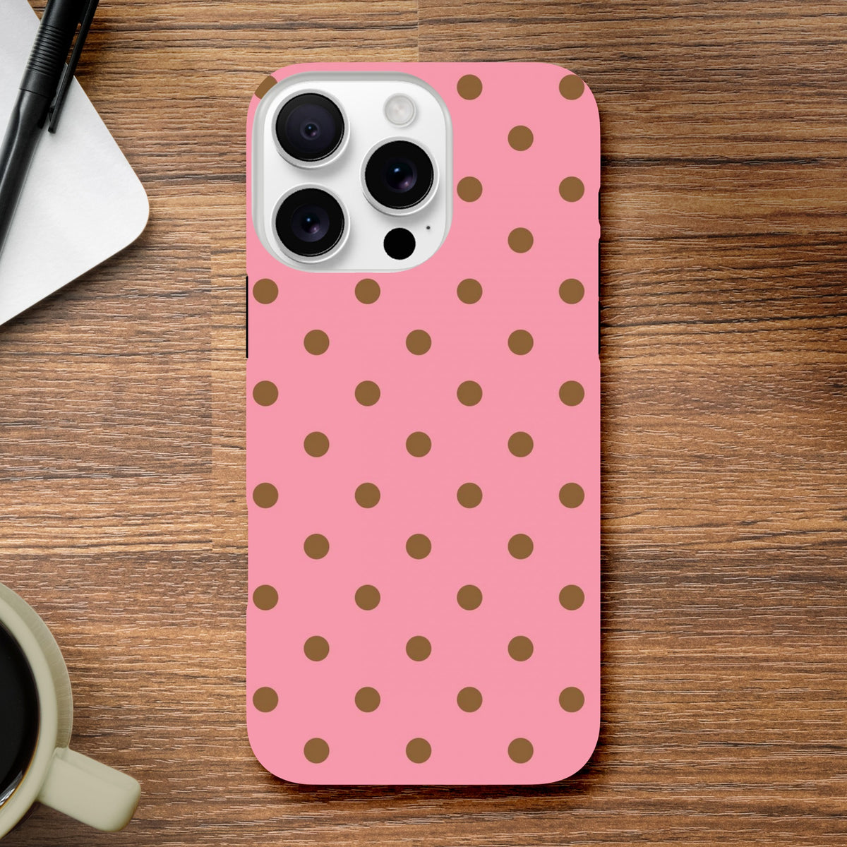 Pink & Brown Polka Dot iPhone Case with shock-absorbing TPU and glossy finish for models 13-16. Cute protective phone cover on wood desk.