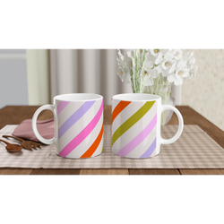 Pastel diagonal stripe ceramic mugs with rainbow diagonals on white, set on a table near a vase of white flowers.