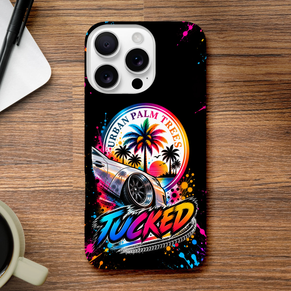 Tucked Petrolhead iPhone case featuring modified car, urban palm trees sunset, and colorful paint splatter on black background.