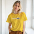 Young woman in a yellow T-shirt with Positive Vibes retro slogan, smiling in a bright hallway.