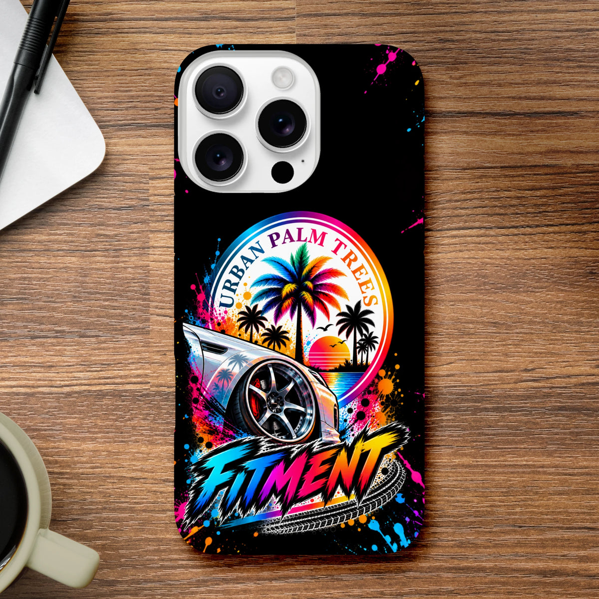 Black iPhone case featuring a colorful lowered modified car, vibrant "Urban Palm Trees" sunset graphic, and bold "Fitment" lettering with paint splatters.