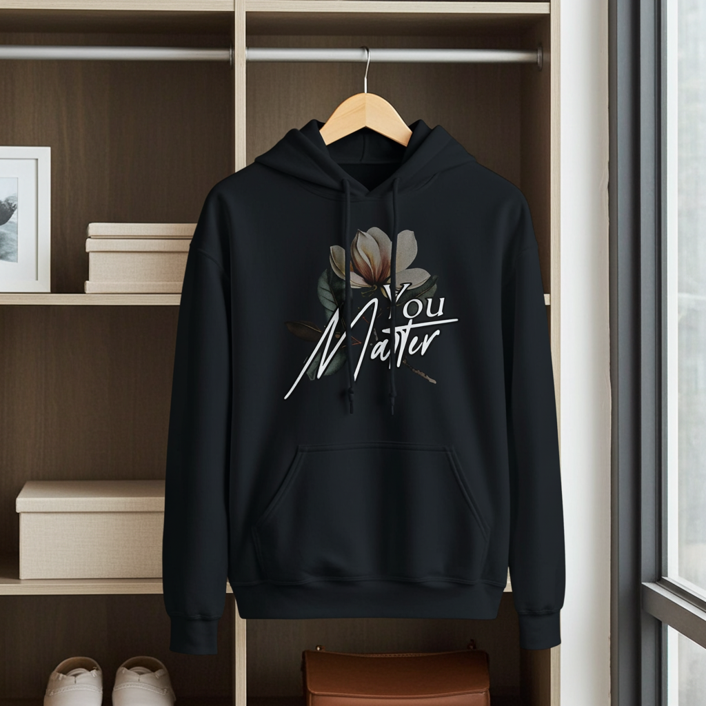 Black hoodie with floral design and text on a hanger against a neutral background