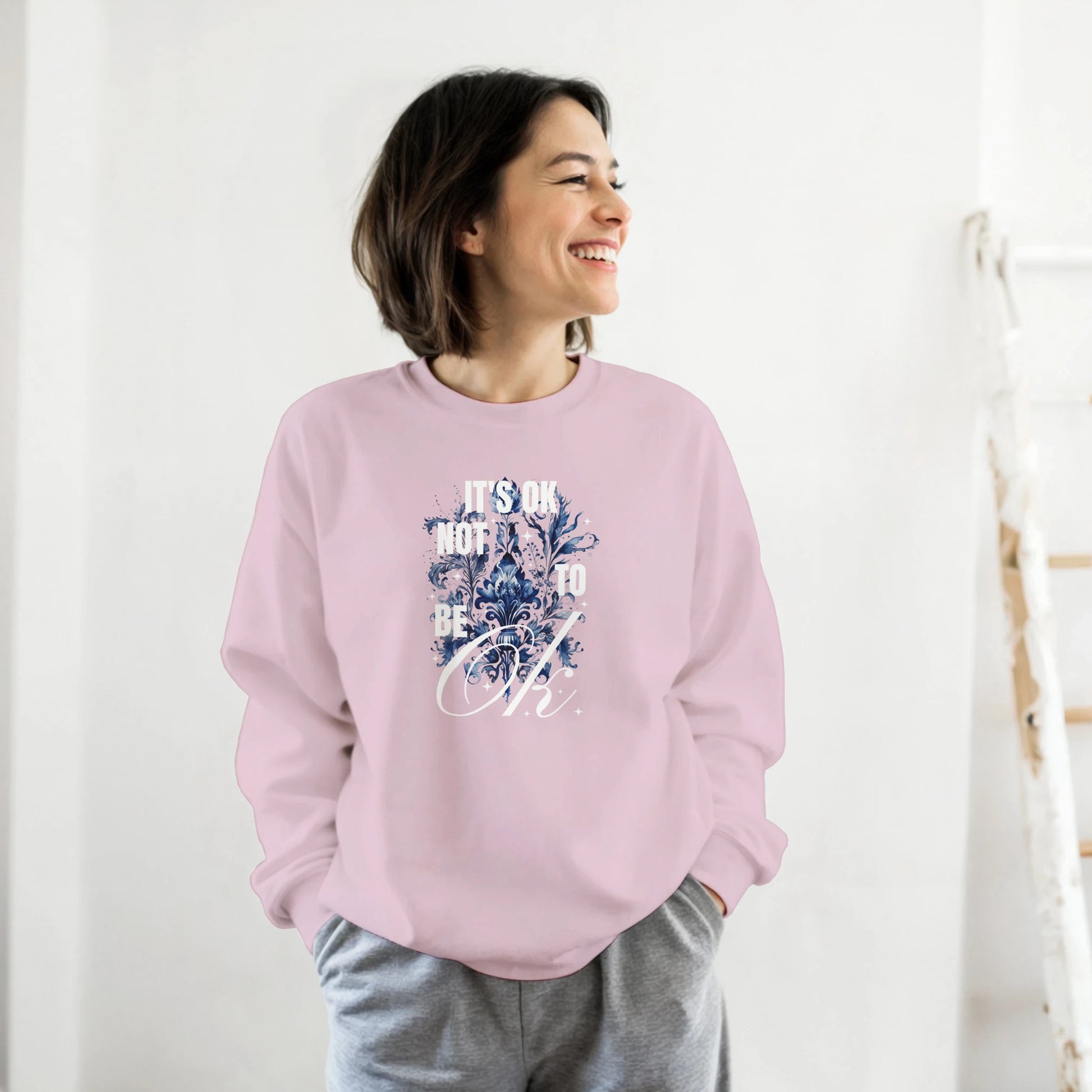 Woman wearing pastel pink Mental Health Jumper graphic sweatshirt with blue design and It's OK Not To Be OK text