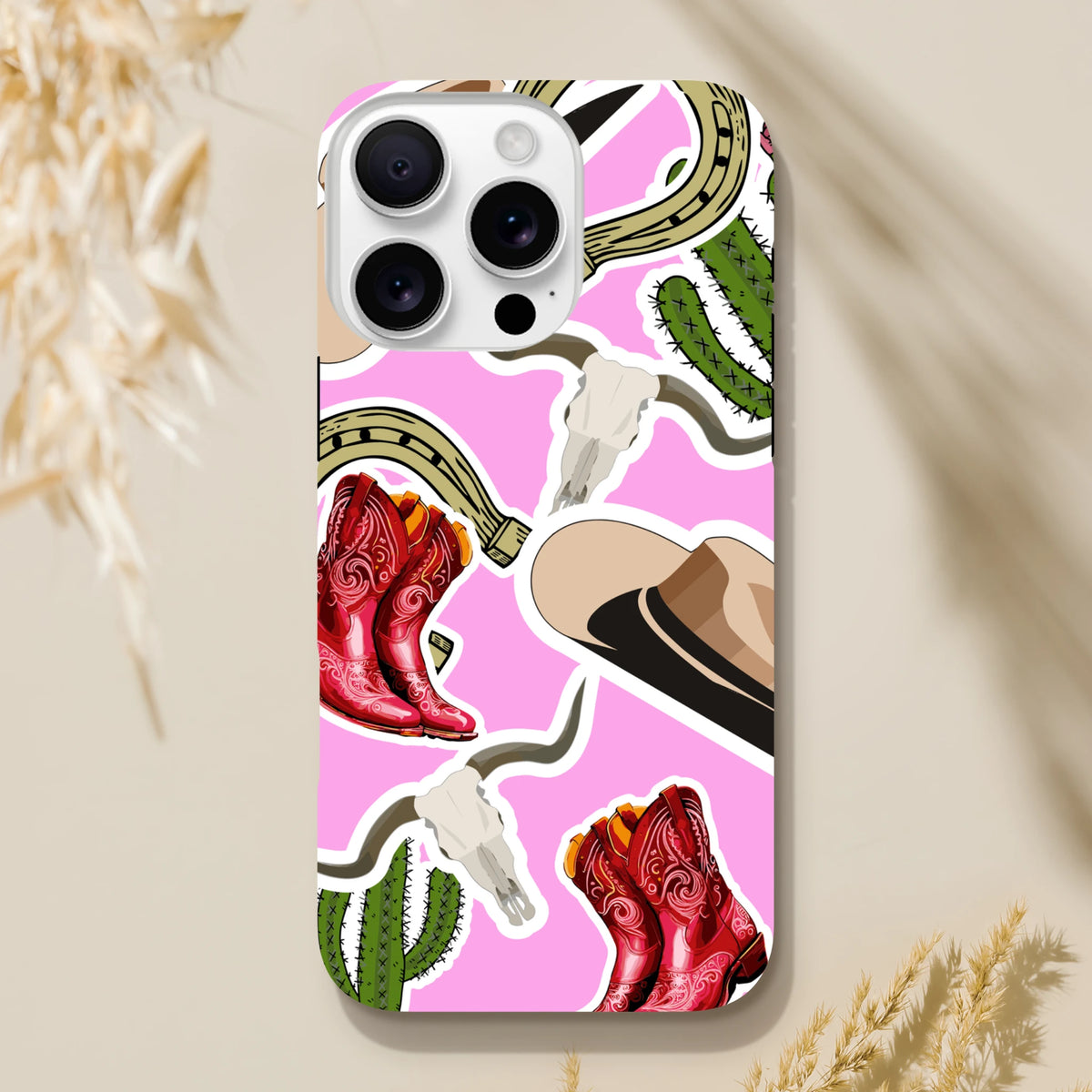Pink western iPhone case featuring red cowboy boots, green cactus, horseshoe, and cowboy hat desert motifs.