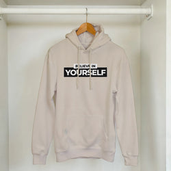 Beige women's Believe In Yourself hoodie on a wooden hanger in a closet.