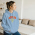 Woman wearing a light blue Berlin Graphic Women’s Hoodie; soft cotton blend, relaxed fit, available in grey, green, blue, sizes S–XL.