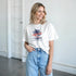 Woman in white California graphic T-shirt with palm tree print; soft cotton blend, casual crew neck.