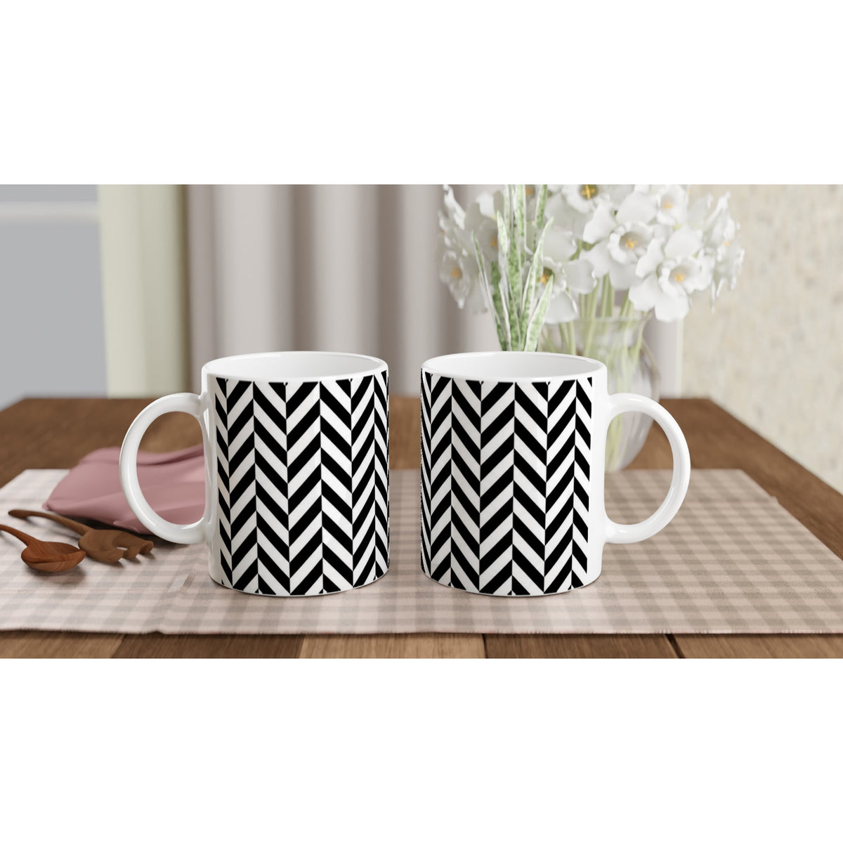 Pair of black and white herringbone ceramic mugs with geometric chevron design on a checkered placemat.