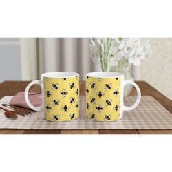 Two yellow ceramic mugs with bee prints on a wooden table, white flowers in the background.