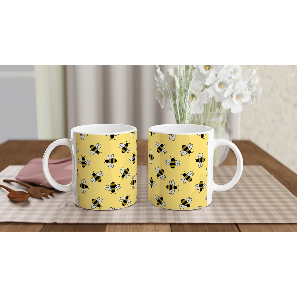 Two yellow ceramic mugs with bee prints on a wooden table, white flowers in the background.