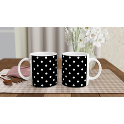 Two black ceramic mugs with white polka dots sit on a wooden table near a vase of flowers. Vintage spotty coffee cups for daily brew.
