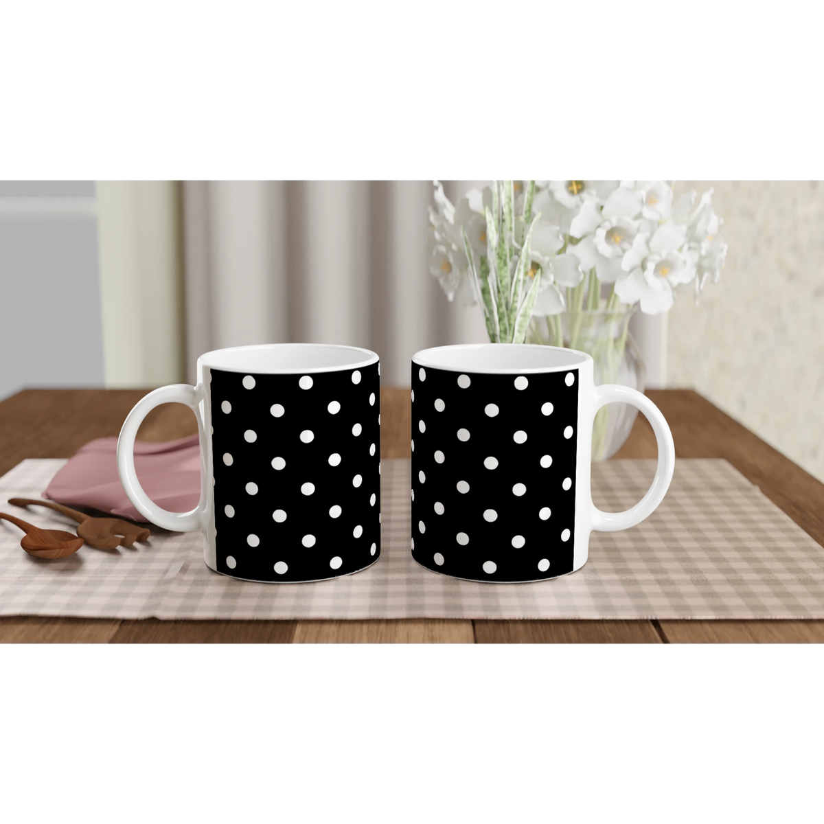 Two black ceramic mugs with white polka dots sit on a wooden table near a vase of flowers. Vintage spotty coffee cups for daily brew.