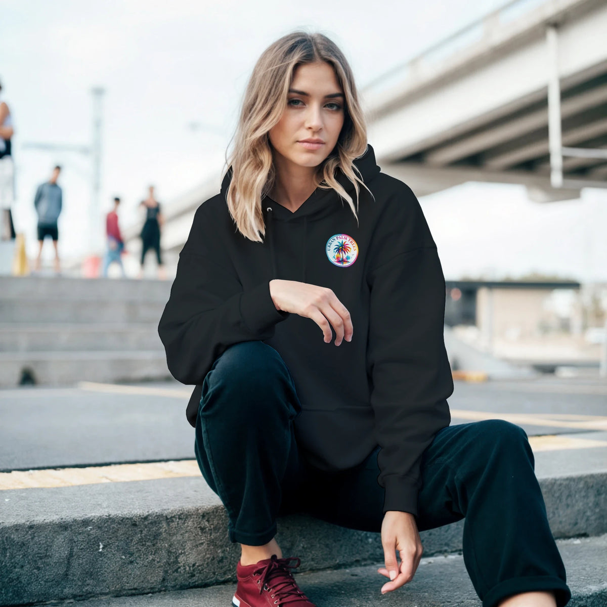 Woman in black tropical retro palm hoodie with small chest logo, relaxed streetwear style with front pouch pocket.