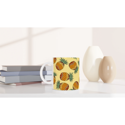 Pineapple-pattern mug, tropical fruit coffee cup on a white desk beside stacked books.