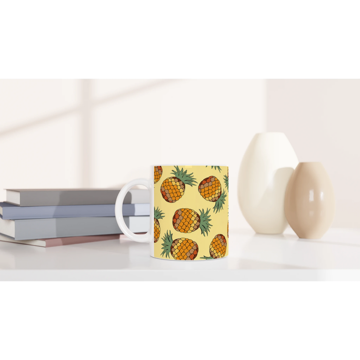 Pineapple-pattern mug, tropical fruit coffee cup on a white desk beside stacked books.