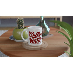 White ceramic mug with Coffee & Chill slogan on a wooden table beside green plants and a cactus.