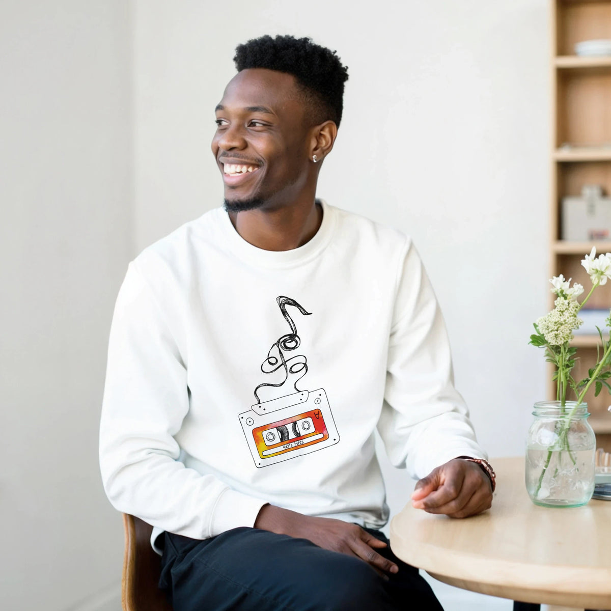 White crewneck sweatshirt featuring a retro cassette tape graphic with unspooling tape and 90s Hits text design.