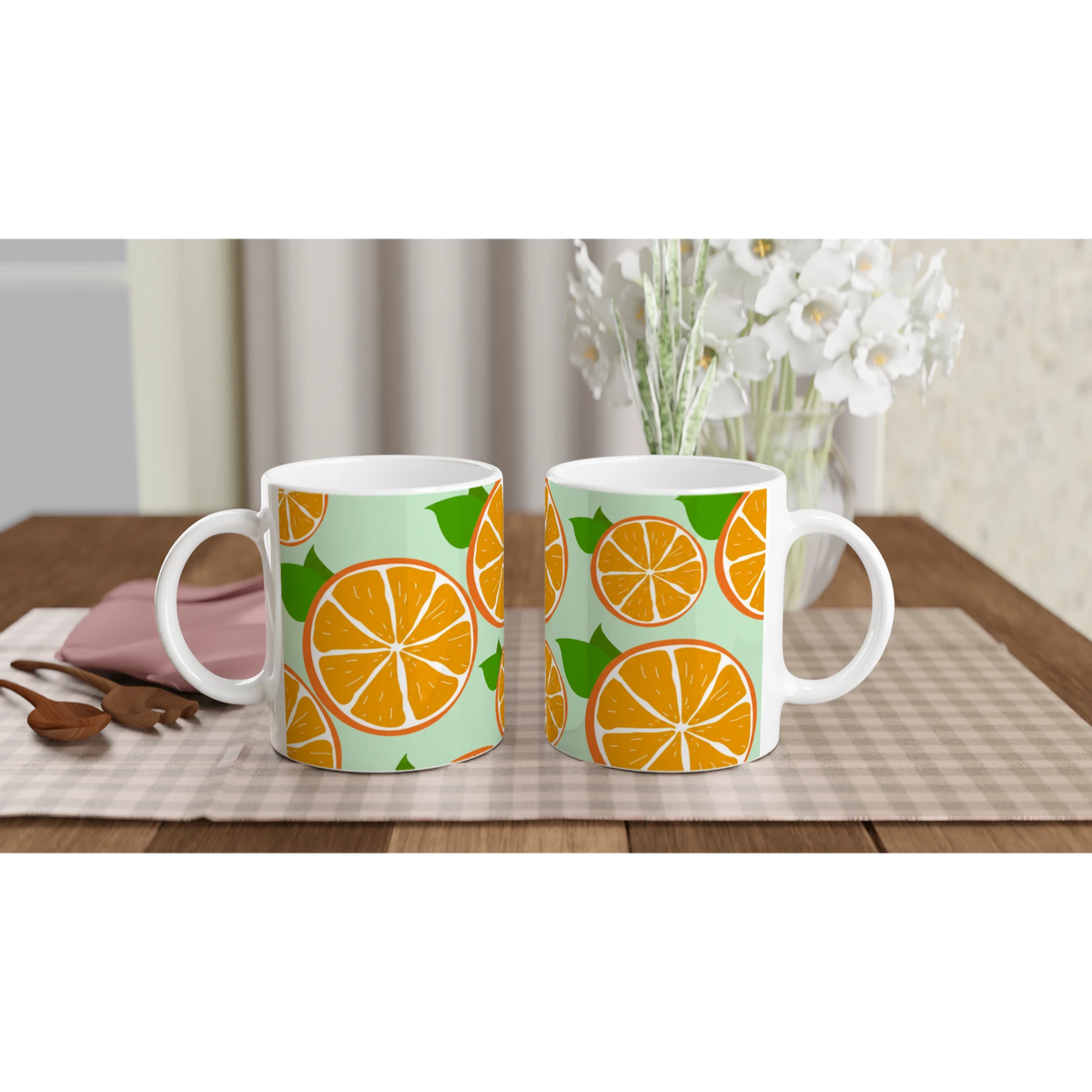 Two mugs with orange slice designs on mint-green backgrounds, placed on a wooden table with a checkered runner.
