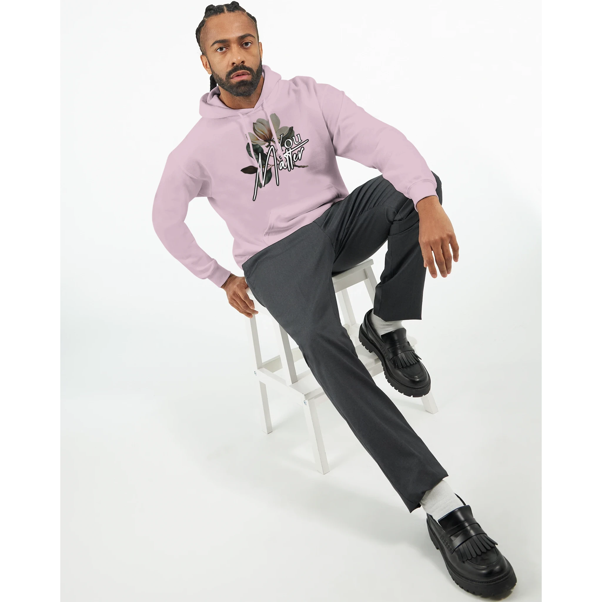 Man wearing pink You Matter slogan hoodie with floral graphic, front pouch pocket, seated on a white stool.