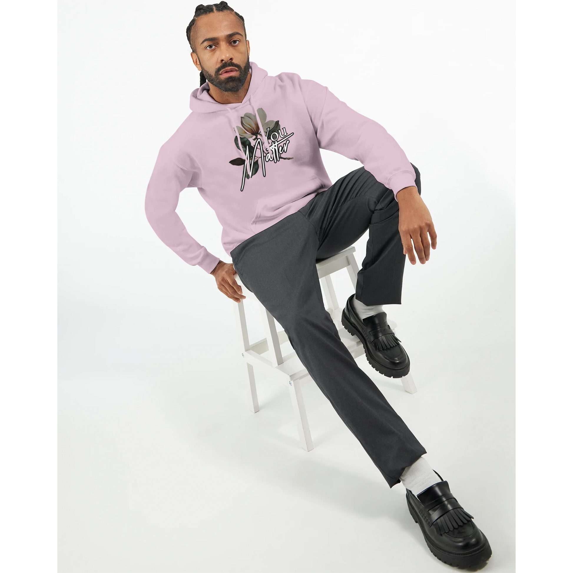 Man wearing pink You Matter slogan hoodie with floral graphic, front pouch pocket, seated on a white stool.