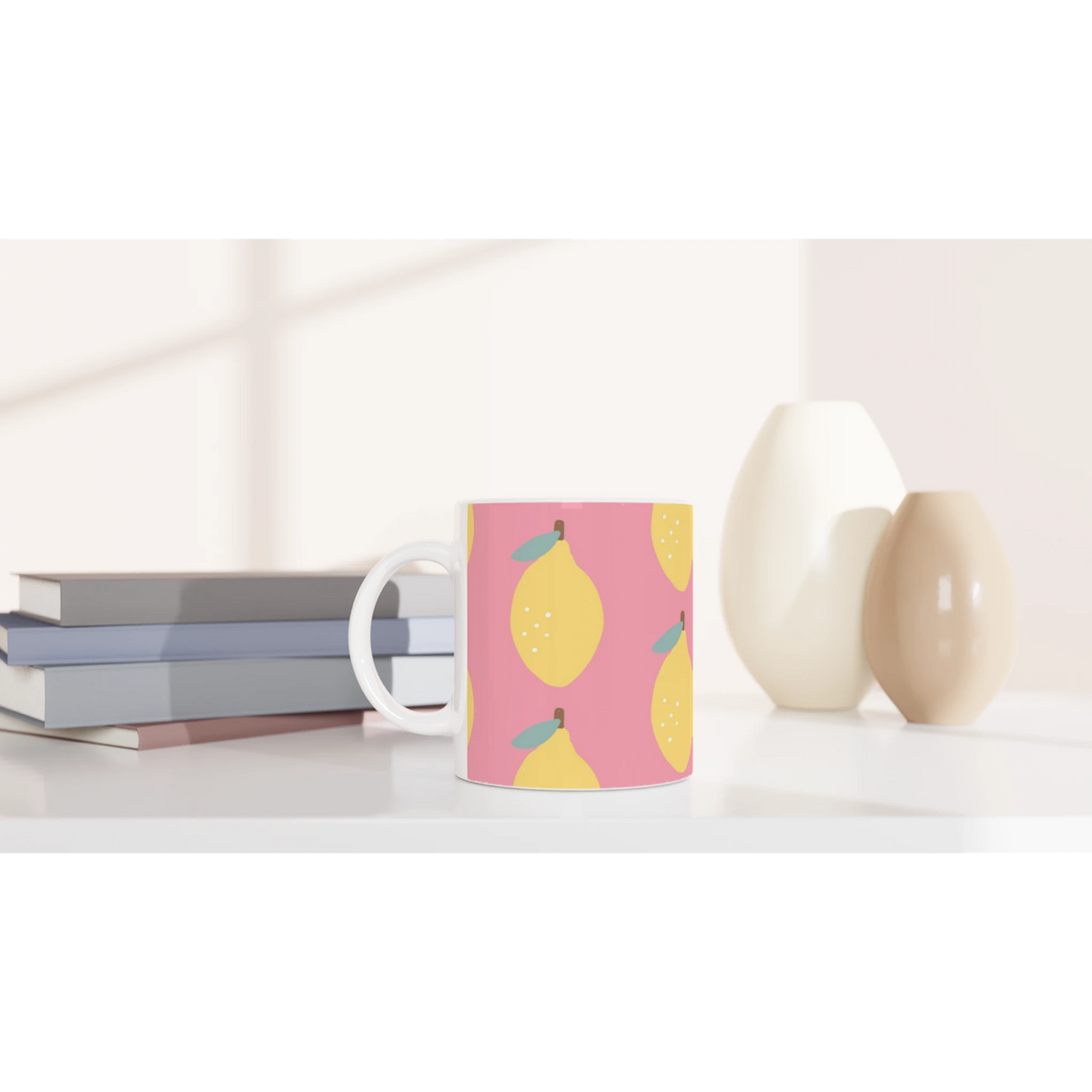 Pink lemon-pattern ceramic mug with yellow lemons and teal leaves, placed on a desk beside books.