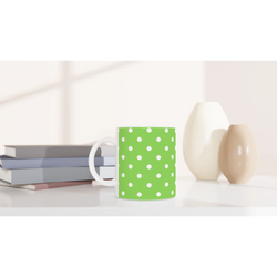 Green and white polka dot ceramic mug sitting on a white desk next to stacked books and minimalist vases.