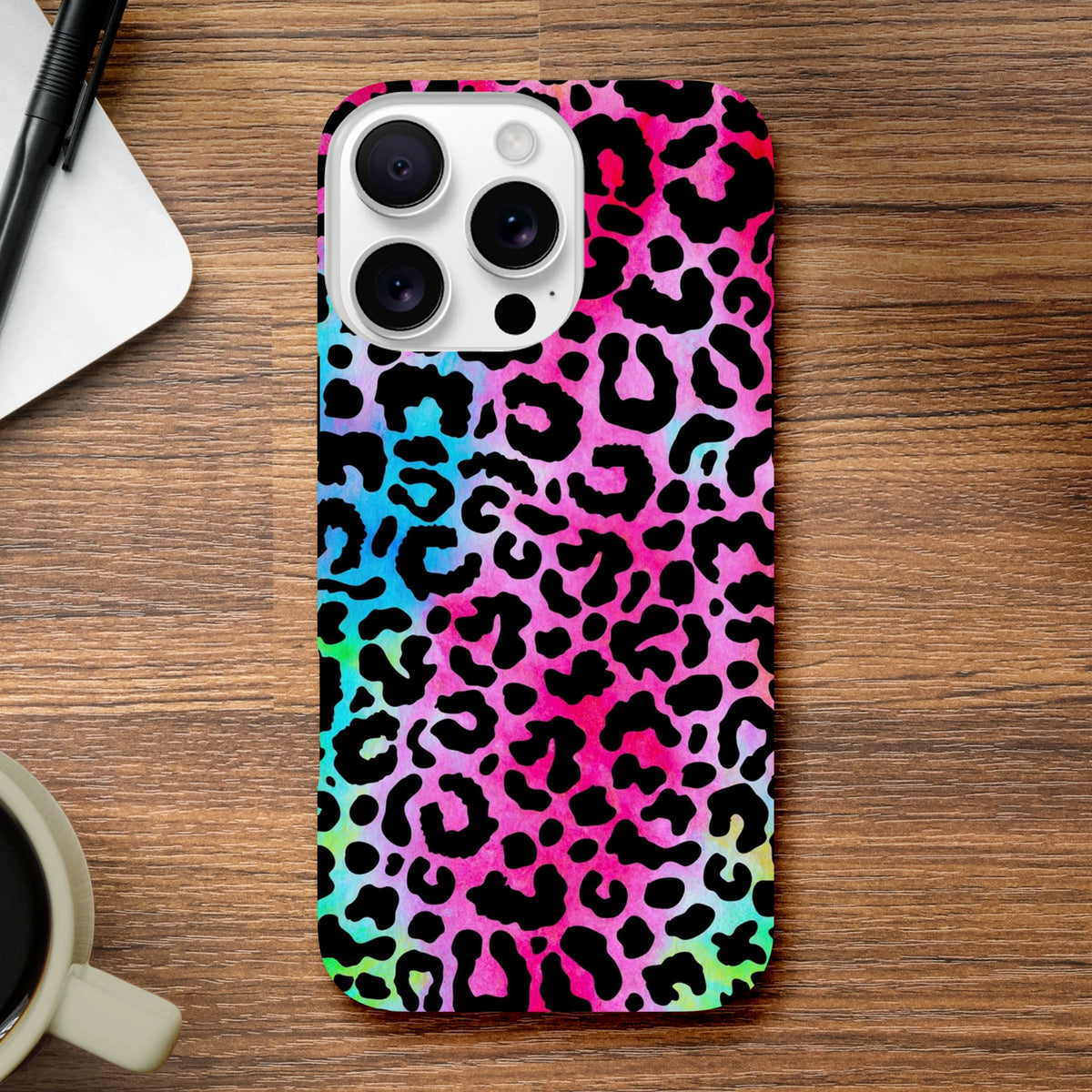 Rainbow leopard print tough iPhone case featuring vibrant animal print protection for iPhone 13-16 series on a wooden desk.