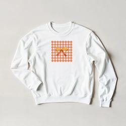 White sweatshirt featuring an orange gingham square graphic with a yellow coquette bow print.