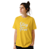 Woman in yellow Stay True T-shirt with retro slogan, urban palm trees vibe.