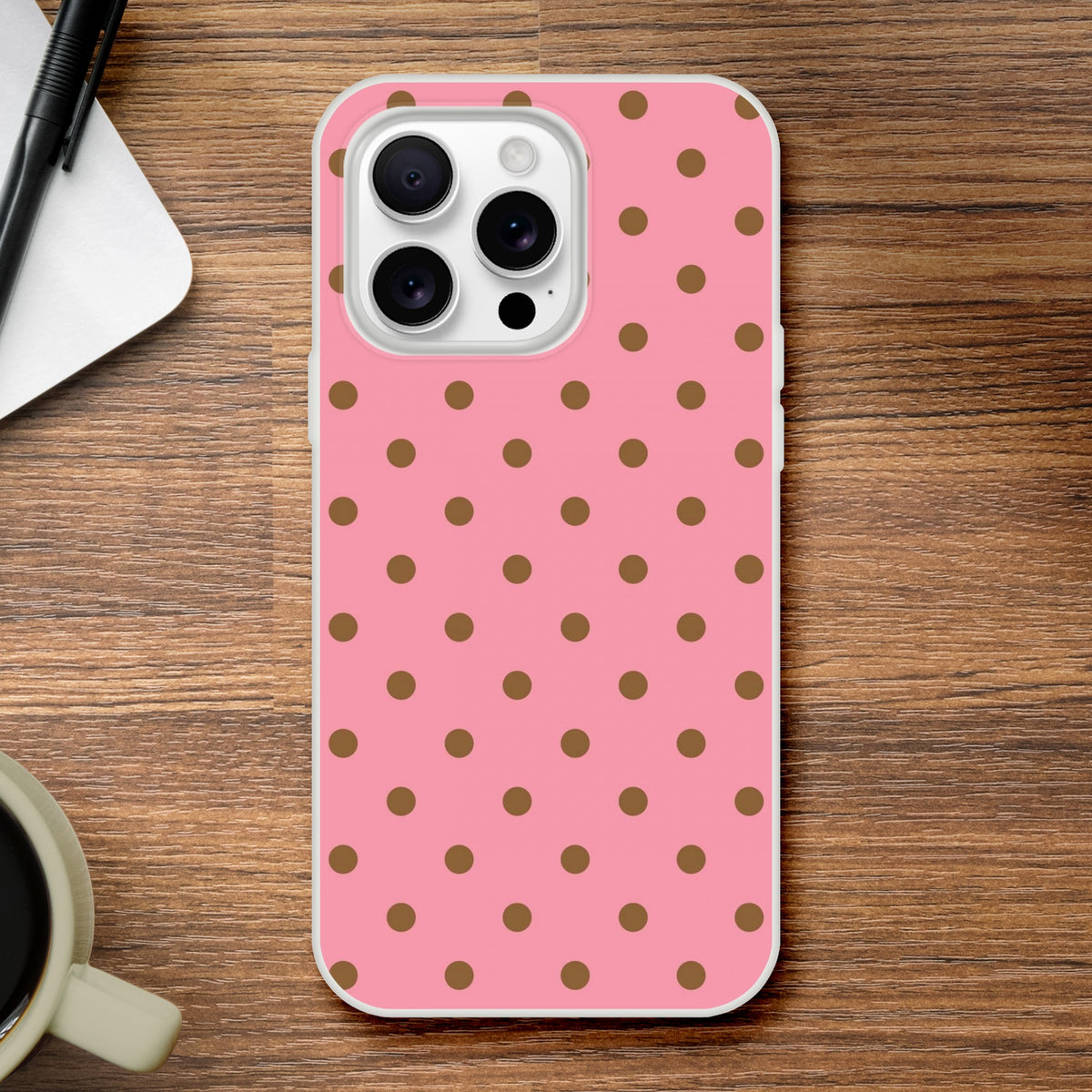 Retro pink and brown polka dot iPhone case providing sleek, low-bulk protection on a wooden desk.