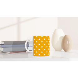 Orange and white polka dot ceramic mug on a desk next to books and vases. Cute spotty coffee cup for daily brews.