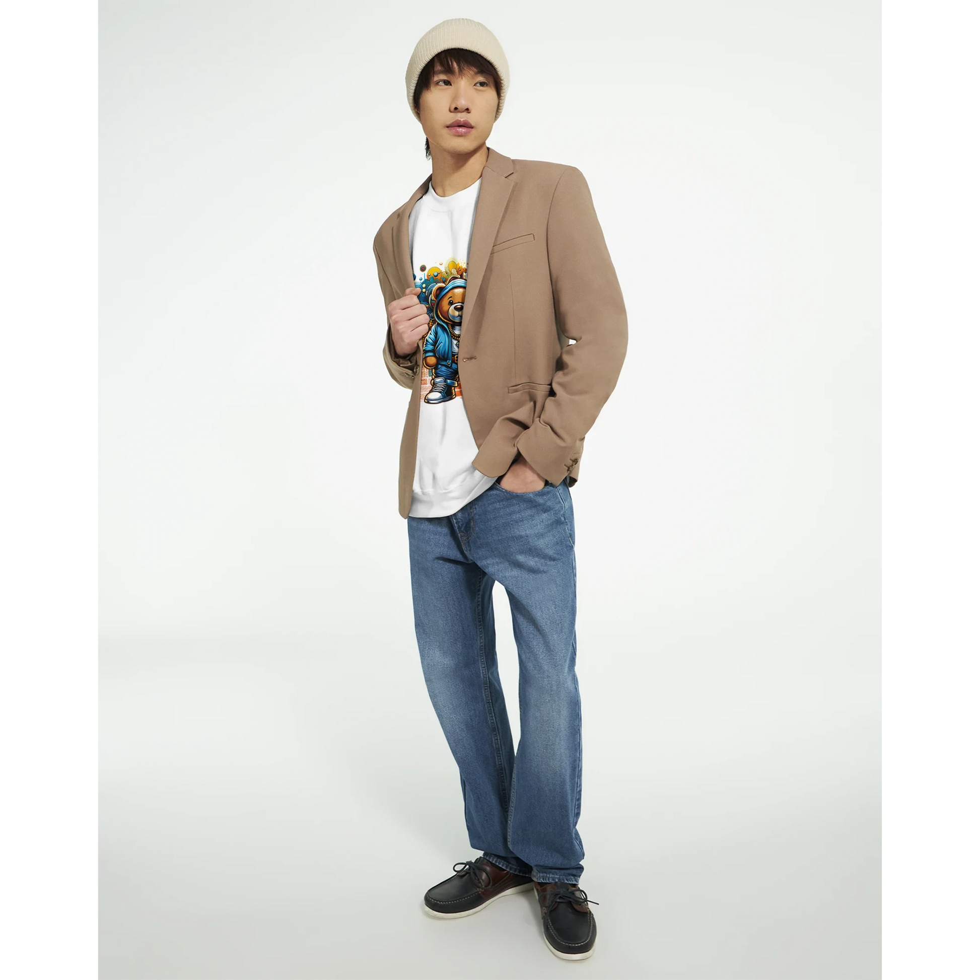 Person wearing a beige blazer, white men's graphic sweatshirt with teddy bear design, blue jeans, and black shoes on a white background