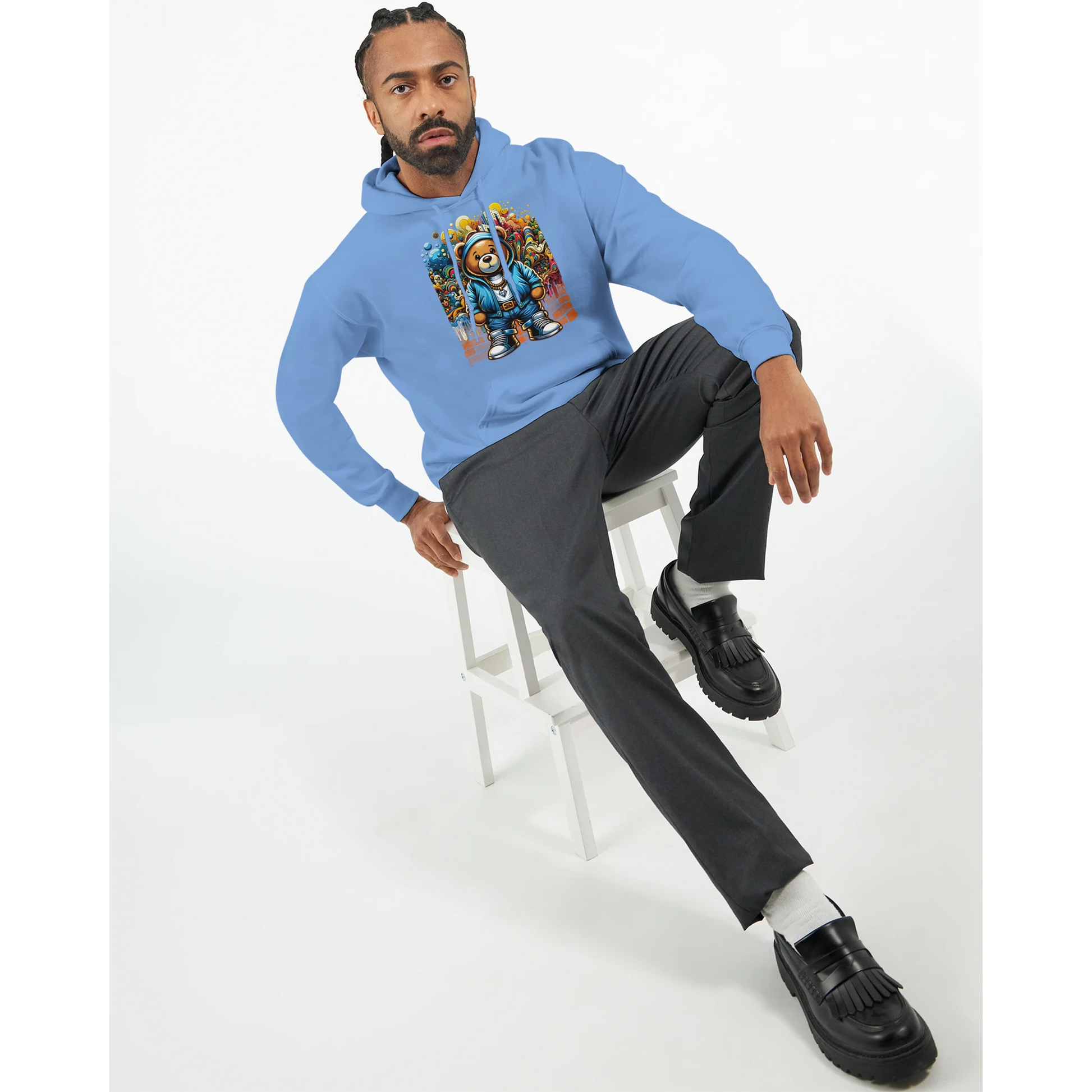 Man wearing a blue men's teddy bear hoodie with a graphic design, sitting on a white stool against a white background.