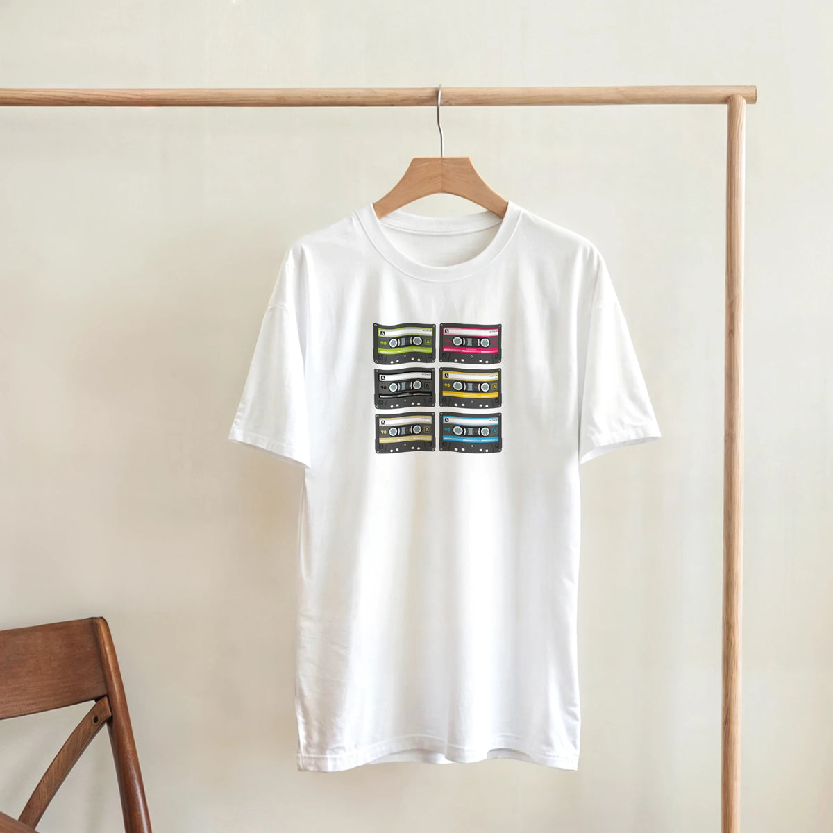 White women's Retro Cassette Collection T-Shirt with stacked colorful cassette tapes on a wooden hanger.