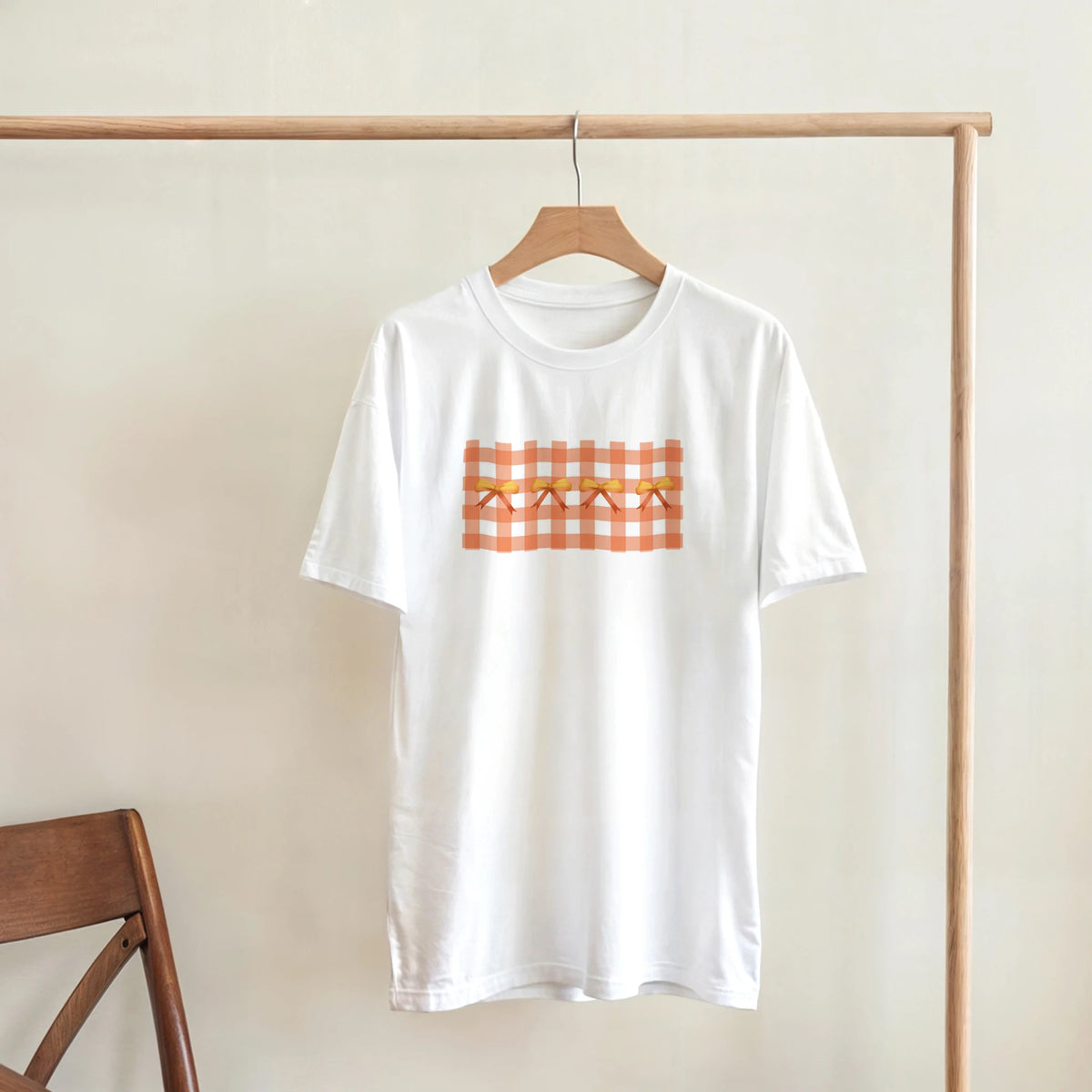 White T-shirt on wooden hanger with orange gingham bow pattern for Coquette aesthetic.