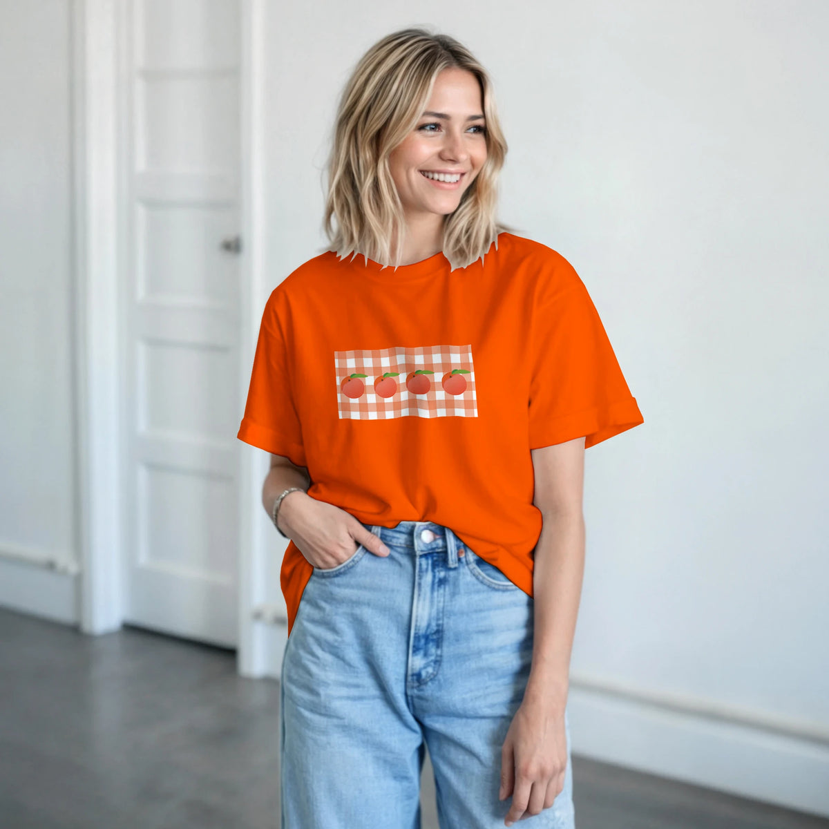 Smiling woman wearing a bright orange T-shirt with a peach gingham graphic on the chest.