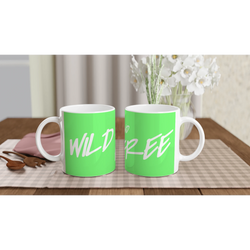 Two green mugs with white cursive slogan on a wooden table, bouquet in blurred background.