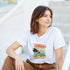 Woman wearing white Tropical Dreamer graphic T-shirt with palm trees and tropical sunset.