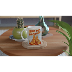 Vintage Barcelona mug with 'Hola from Barcelona' postcard design on a wooden table beside a cactus.