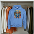 Blue hoodie with a colorful bear design hanging on a rack among other sweaters.