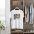 White t-shirt with 'Miami' graphic design hanging on a rack in a room with shelves and plants.