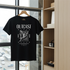 Black t-shirt with 'OUTCAST' design on a hanger by a window with a city view.