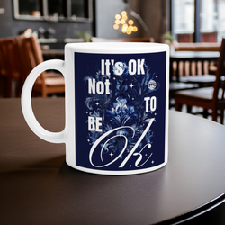 White mug with a blue design and text on a table in a room with chairs and a window.