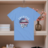 Blue t-shirt with 'American Girl' graphic on a hanger against a neutral background