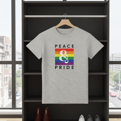 Gray t-shirt with 'Peace & Pride' design on a hanger in front of a window.